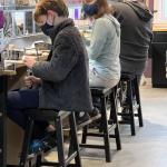 Photograph of three people wearing masks, working at stools in a bright, purple-walled workshop.