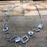 Photograph of a silver chain necklace with geometric shapes on a wooden surface.