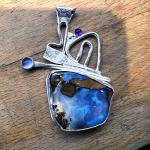 Photograph of an abstract silver pendant with a blue boulder opal and small purple stones.