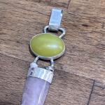 Photo of a silver pendant with a green and light pink stone on a wooden surface.