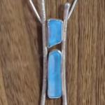 Photograph of a silver pendant with two blue sea glass pieces against a wooden background.