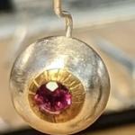 Photograph of a silver and gold earring featuring a round ruby gemstone.
